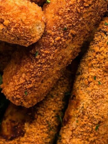 A close-up of several breaded mozzarella sticks arranged next to a small bowl of marinara sauce.