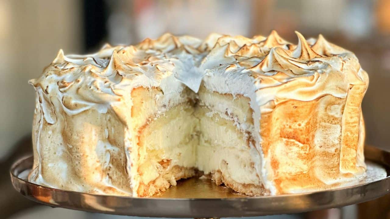 A Baked Alaska cake with a toasted meringue exterior and a visible cross-section showing layers of cake and ice cream on a round tray.