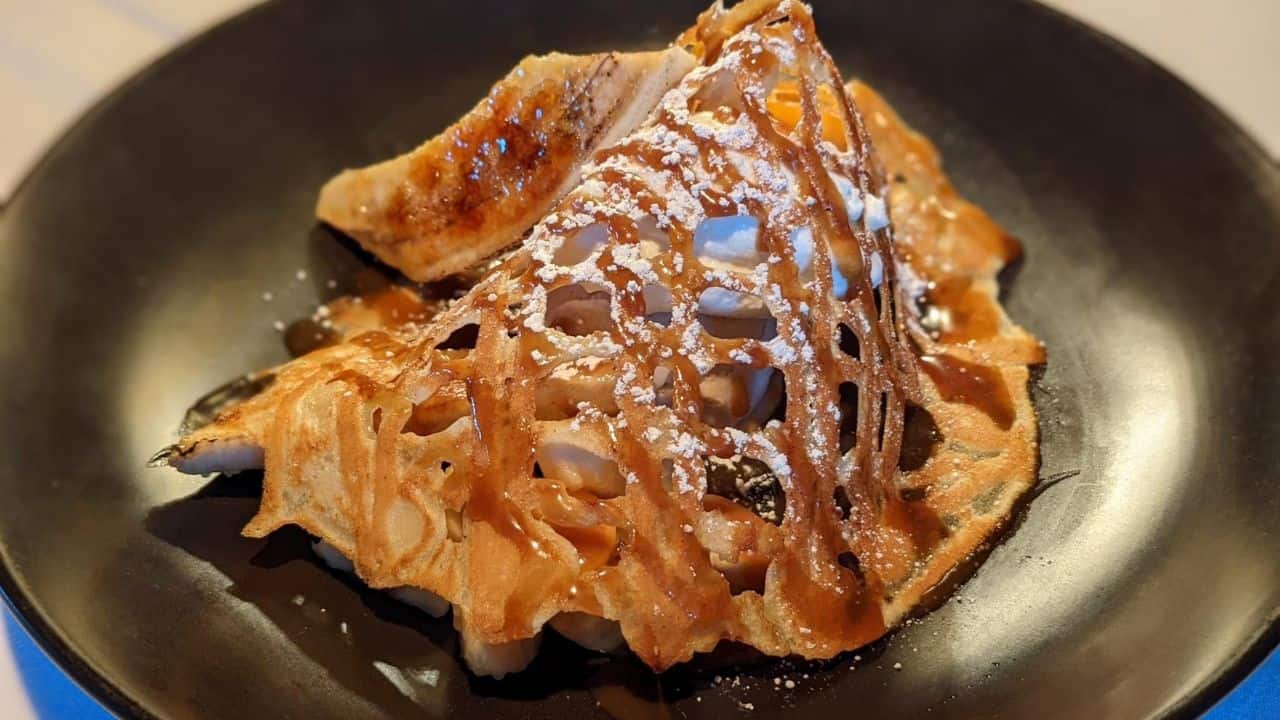 A folded crepe topped with a caramelized drizzle and powdered sugar sits on a black plate.