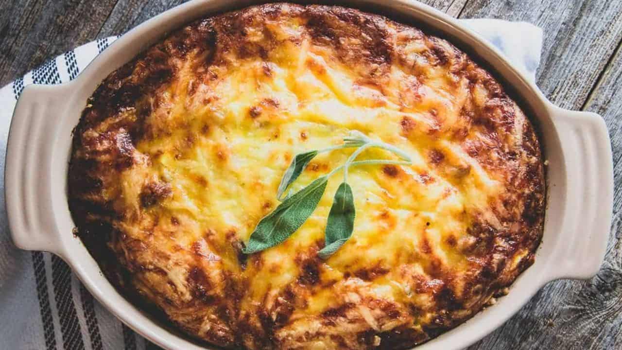 Cheesy potato and sausage casserole in a baking dish on wooden surface.