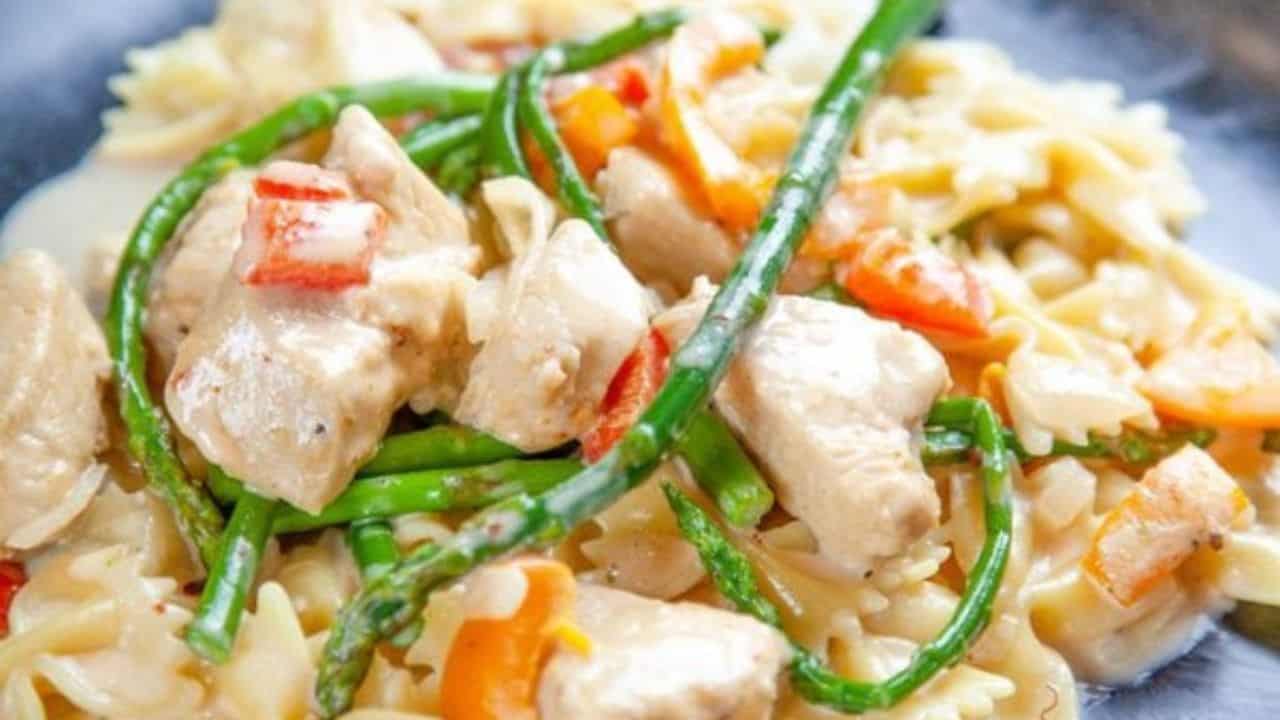 A close-up of pasta with pieces of chicken, asparagus, and red bell peppers in a creamy sauce.