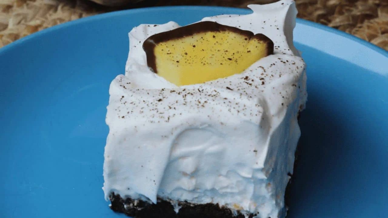 A piece of chocolate covered dessert on a plate next to a pan of dessert.