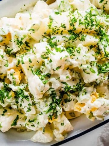 A bowl of classic potato salad topped with chopped fresh herbs, served in a white dish with a blue rim.