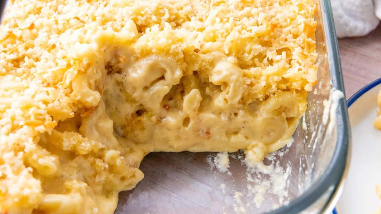 A baking dish filled with creamy macaroni and cheese, topped with a golden breadcrumb crust, with a portion served out.