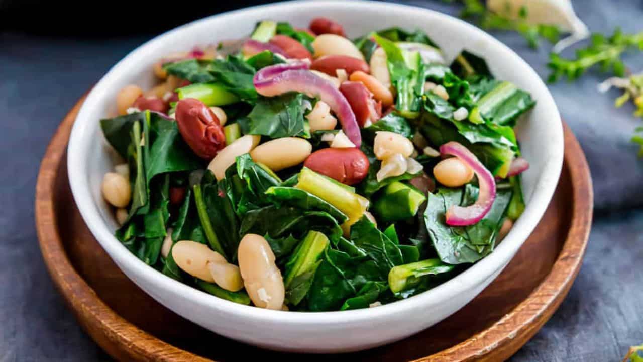 Beans and greens in a skillet with a wooden spoon.