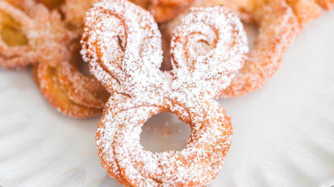 A bunny-shaped pastry topped with powdered sugar is placed on a white plate with other pastries in the background.