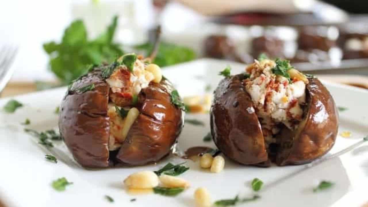 Goat cheese stuffed baby eggplants on a white plate with parsley and pine nuts.
