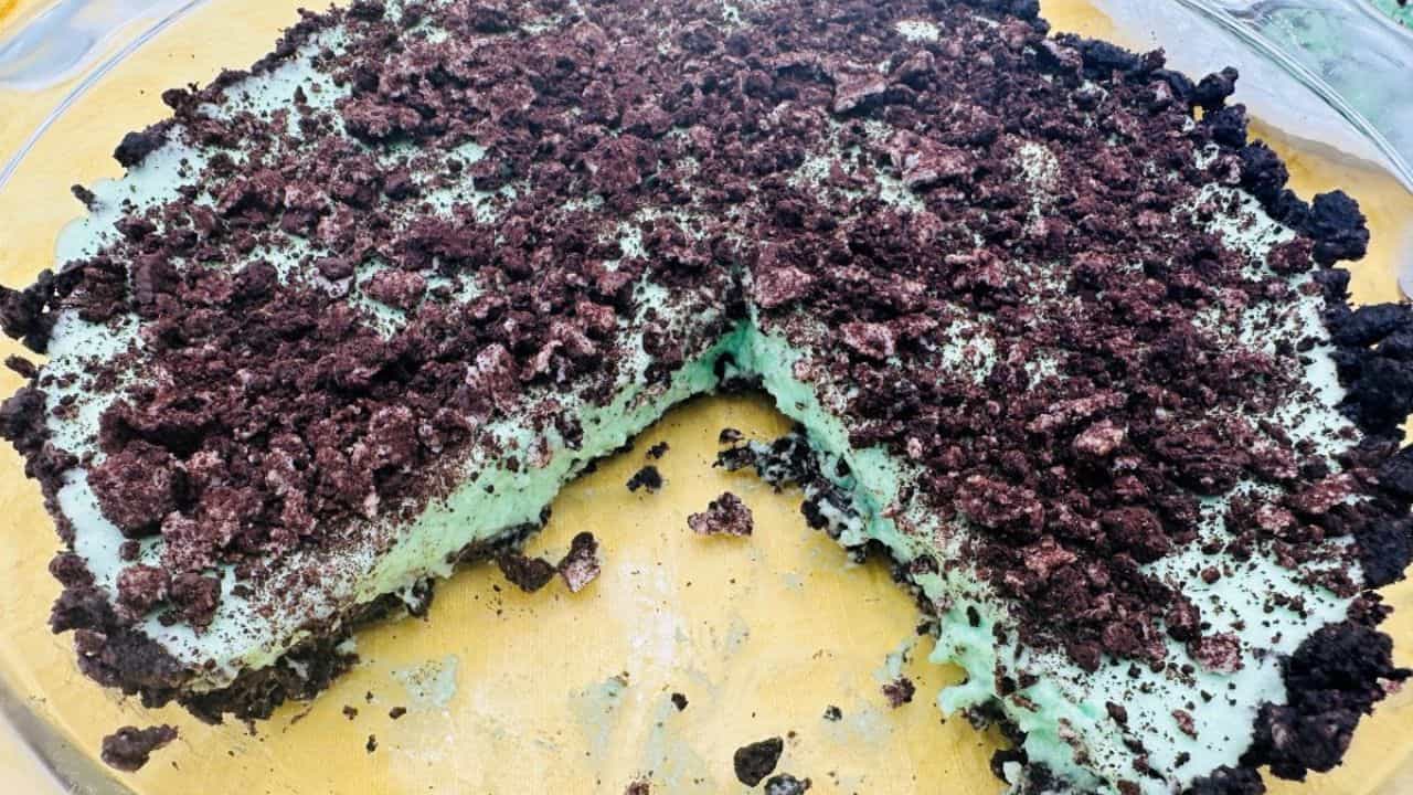 A slice of green oreo pie on a plate with a fork.