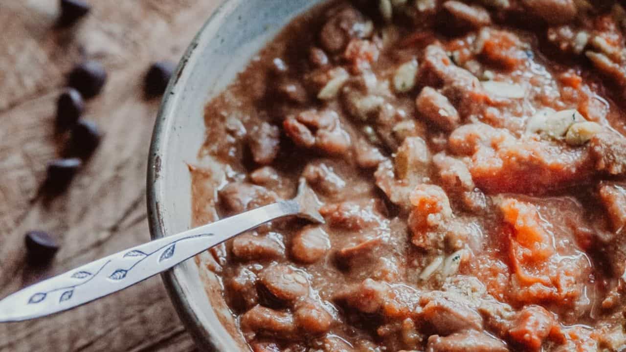 Close-up of a bowl of chili with beans, tomato chunks, and a silver spoon resting inside the bowl.