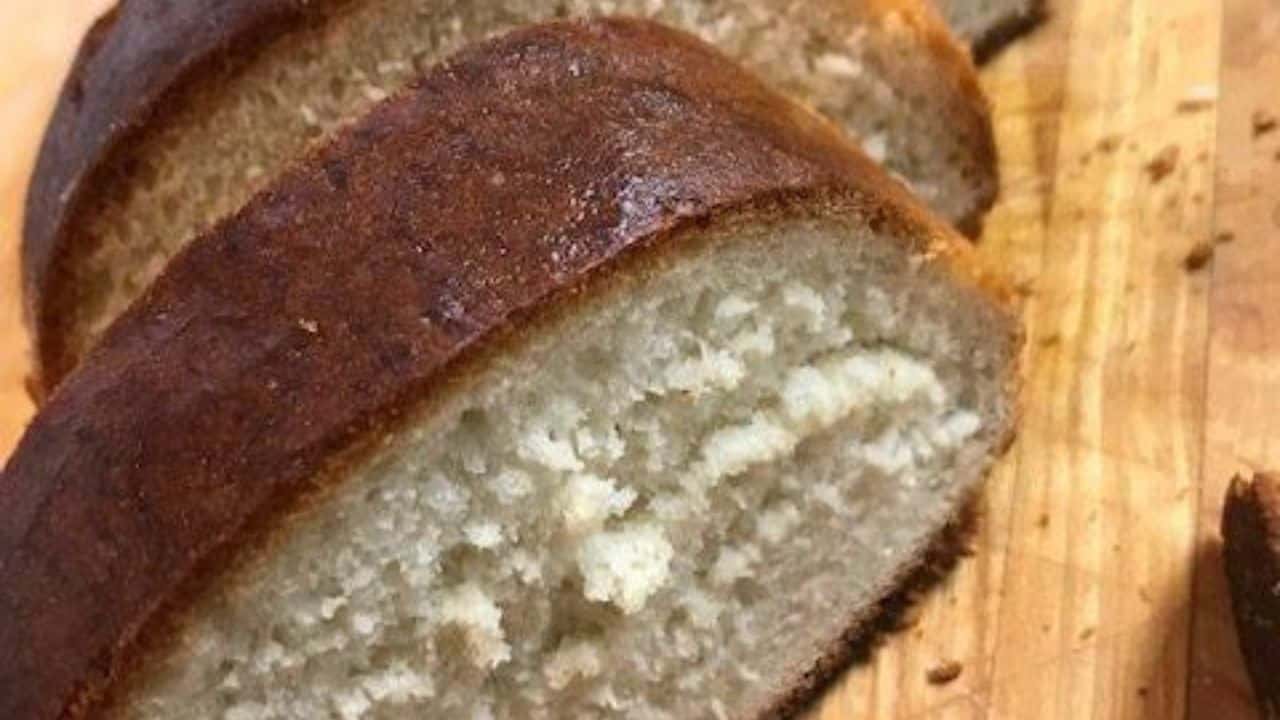 A sliced loaf of white bread rests on a wooden surface, revealing its light, fluffy interior and golden crust.