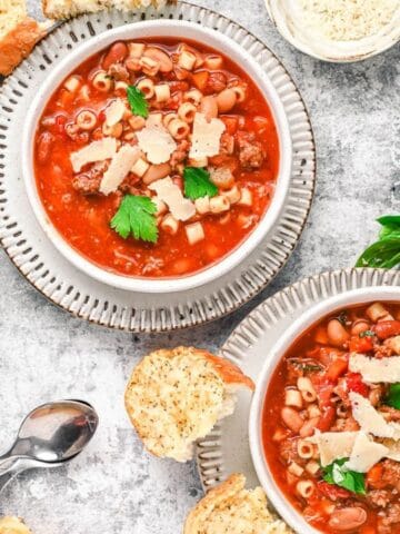 Three bowls of minestrone soup topped with parsley and parmesan, served with slices of bread; a slow cooker and grated cheese are nearby.