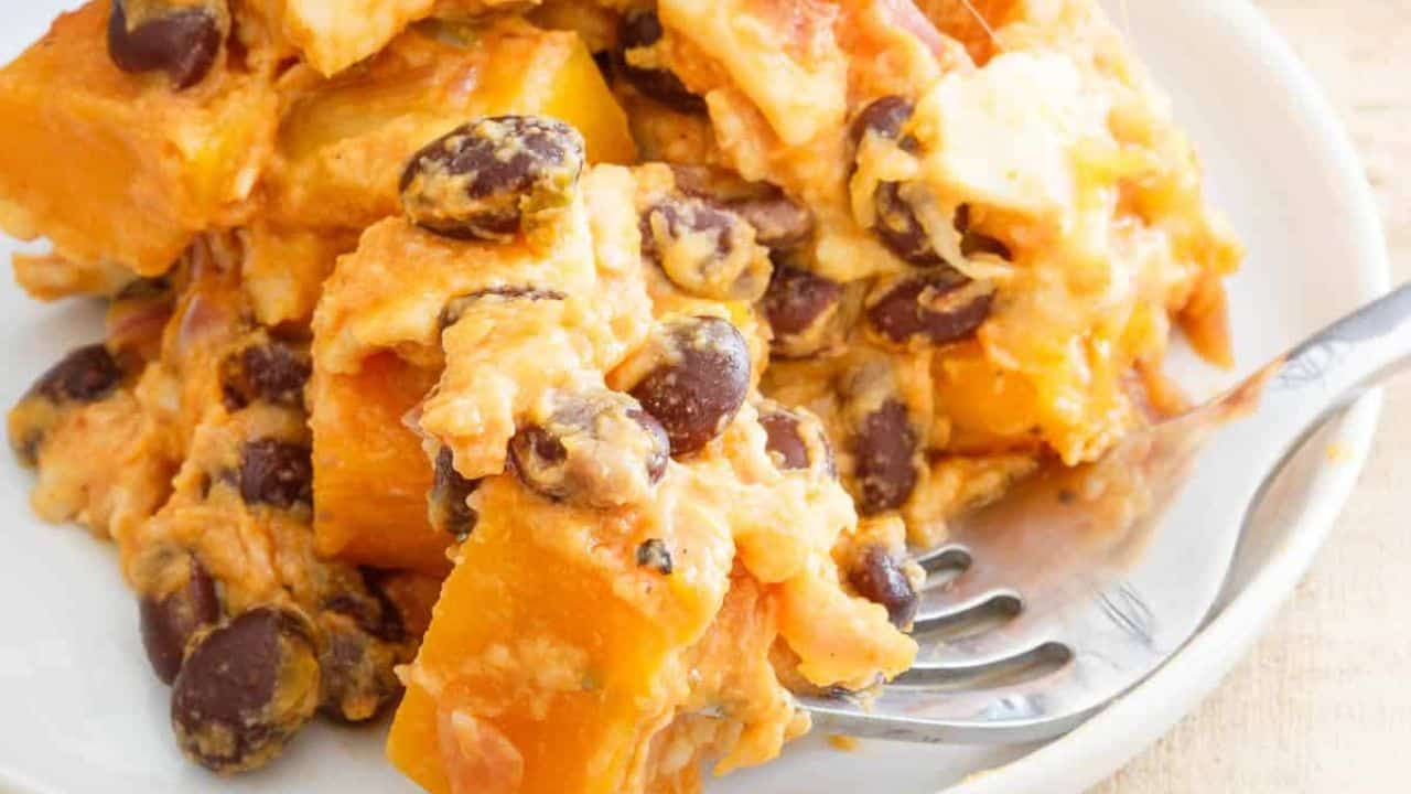 Pumpkin tortilla casserole in a baking dish with wooden serving spatula topped with jalapenos.