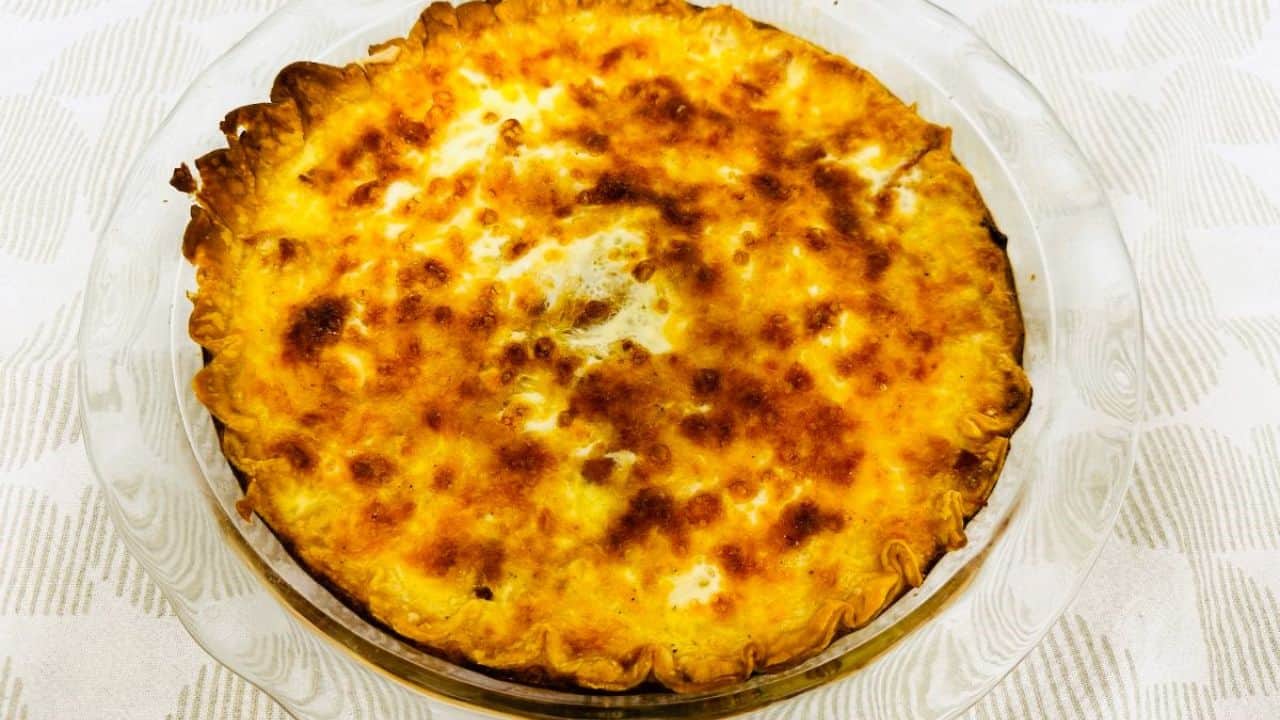 Slice of Quiche Lorraine on white plate next to fork and green salad.