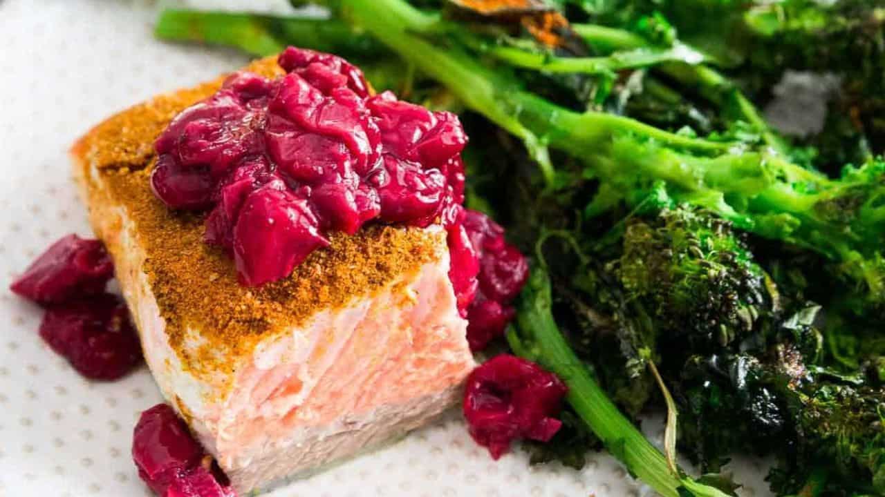 Turmeric salmon with cherry sauce and roasted broccoli rabe on a plate.