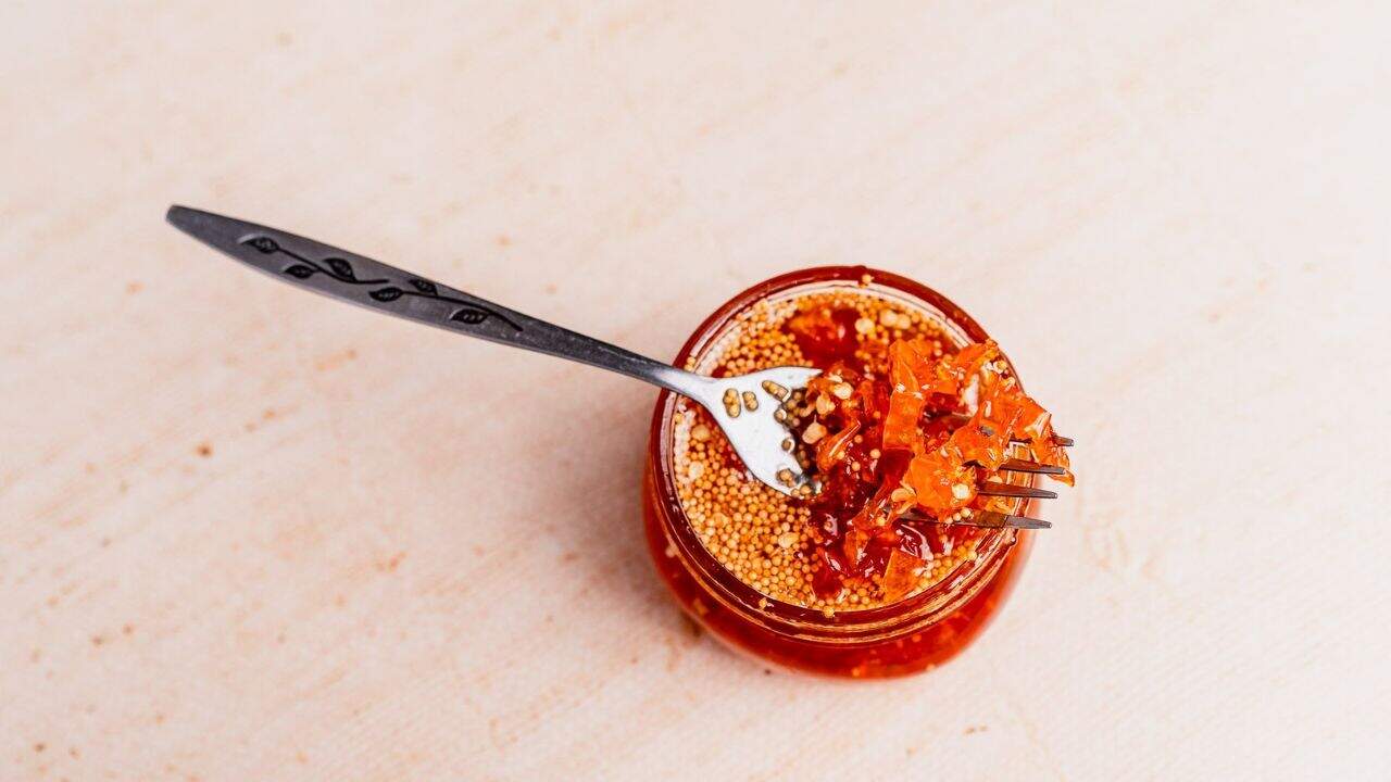 A small glass jar filled with chili oil and visible seeds, with a fork resting on top and holding a portion of the chili condiment.