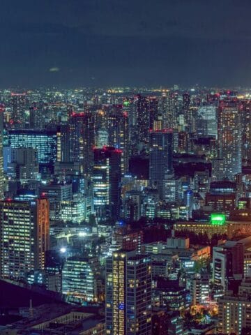 A nighttime cityscape of Tokyo with the illuminated Tokyo Tower standing out among tall buildings and city lights.