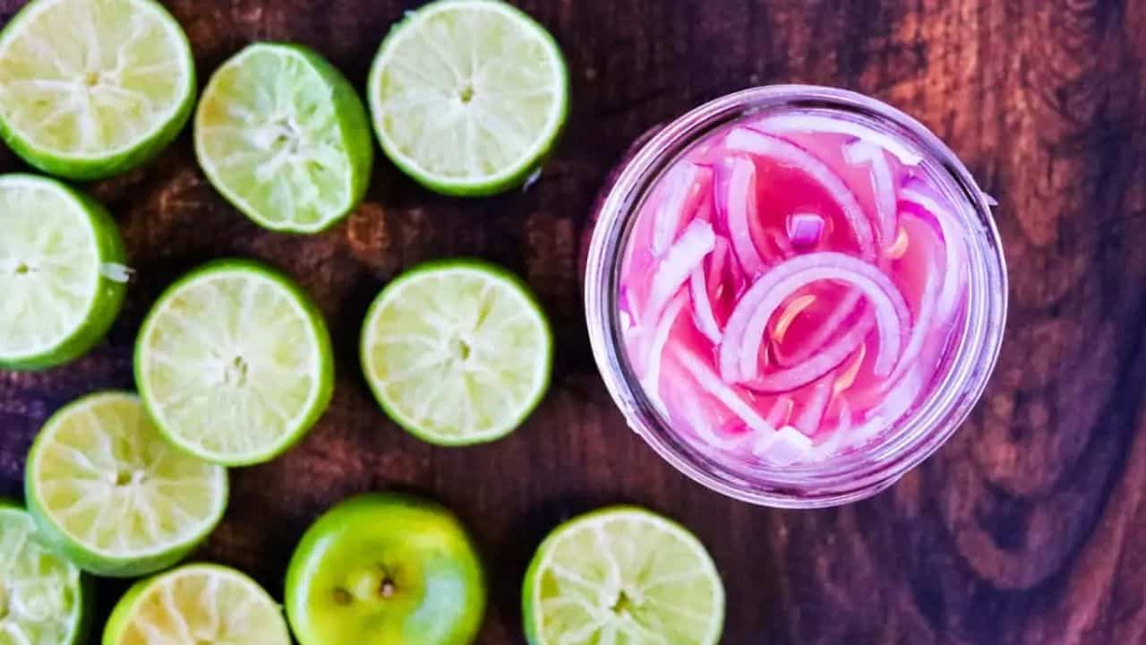 Overhead shot of a jar of pink pickled onions with lime halves on the side.