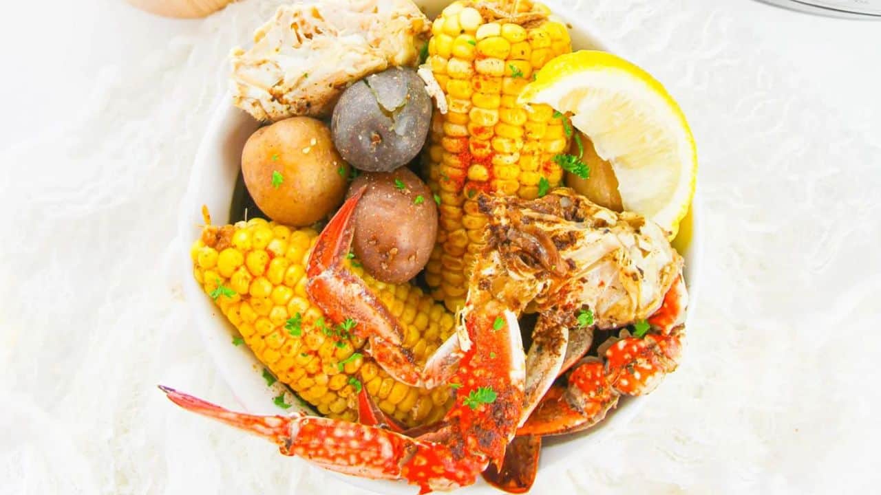 A bowl containing crab legs, corn on the cob, potatoes, and a lemon wedge, garnished with chopped parsley.