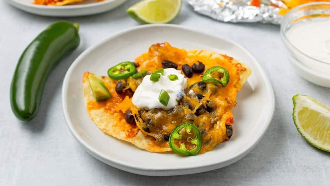 A close-up imag of loaded nachos topped with melted cheese, avocado chunks, black beans, diced tomatoes, green onions, and dollops of sour cream.