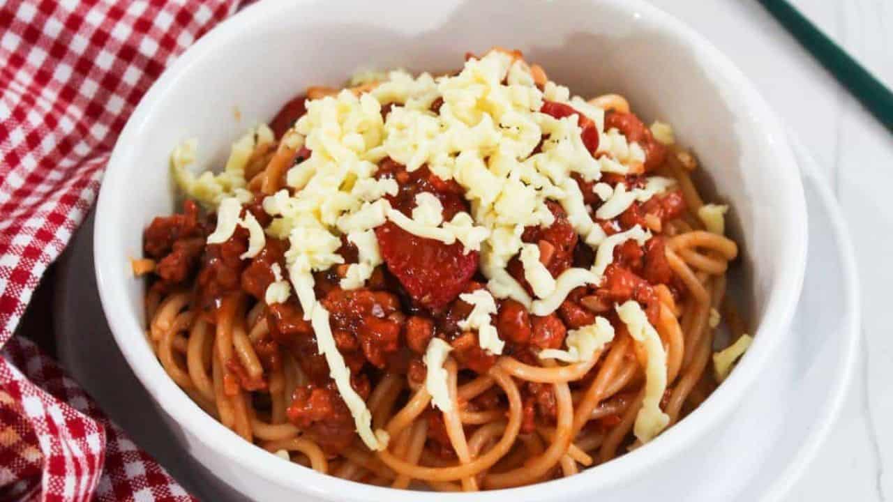 A bowl of spaghetti topped with a rich meat sauce placed on a red and white checkered tablecloth.