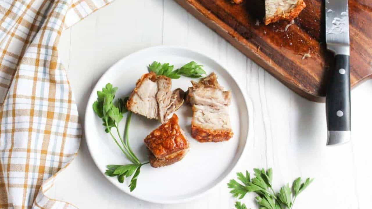 A basket of crispy roasted pork belly chunks garnished with parsley, served in a white paper-lined wicker basket.