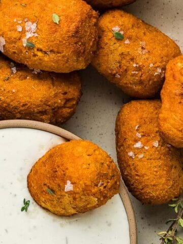A plate of golden-brown croquettes garnished with herbs, served with a bowl of creamy dipping sauce on the side.