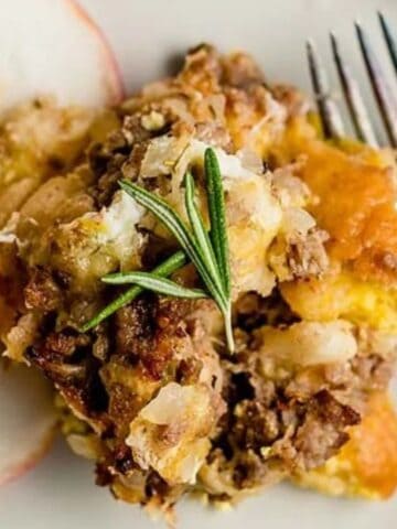 A serving of casserole topped with ground meat and herbs is served on a plate with two apple slices and a fork.
