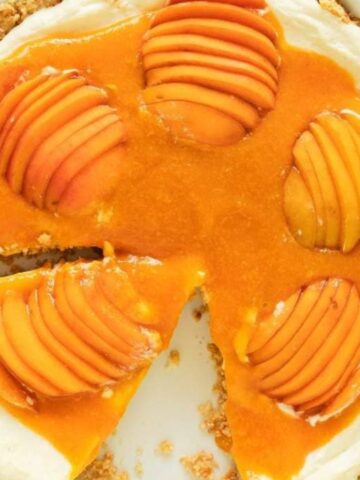 A tart with a crumbly crust, creamy filling, and sliced apricots arranged on top; one slice has been removed.
