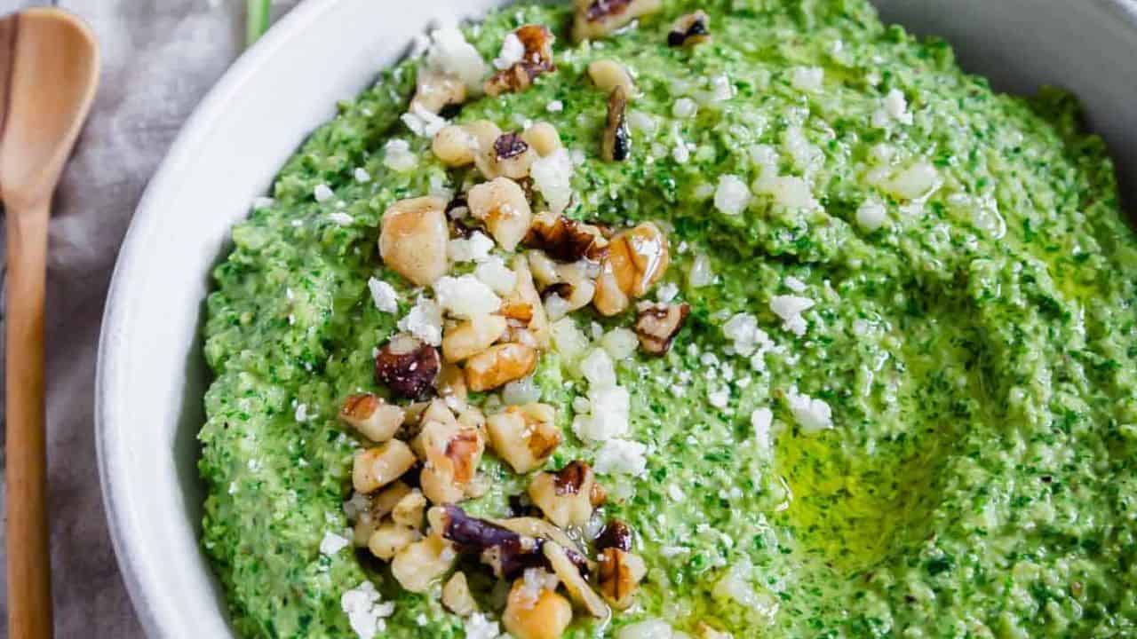 A bowl of green arugula pesto on a wooden table.