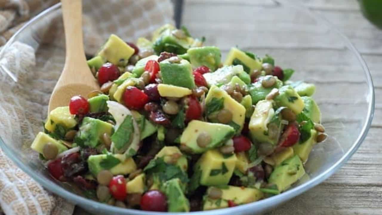 Avocado lentil salad in a bowl with serving spoon and silver plate with fork.