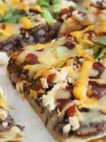 A close-up of sliced flatbread topped with melted cheese, beans, chopped green onions, cilantro, and a drizzle of sauce.