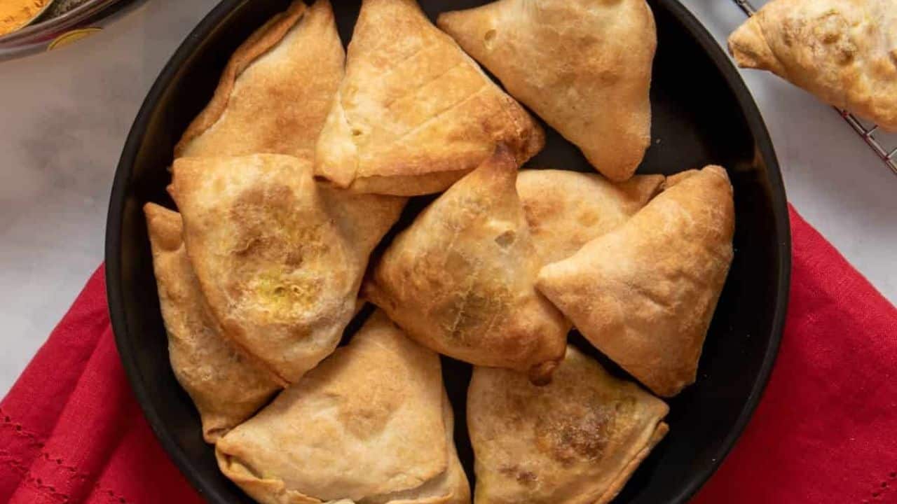 Top view image of healthy samosas on a black plate with additional samosas on a cooling rack.