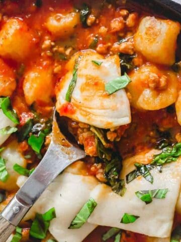 A skillet filled with gnocchi, tomato sauce, stuffed pasta shells, and fresh basil, partially served with a metal spoon.