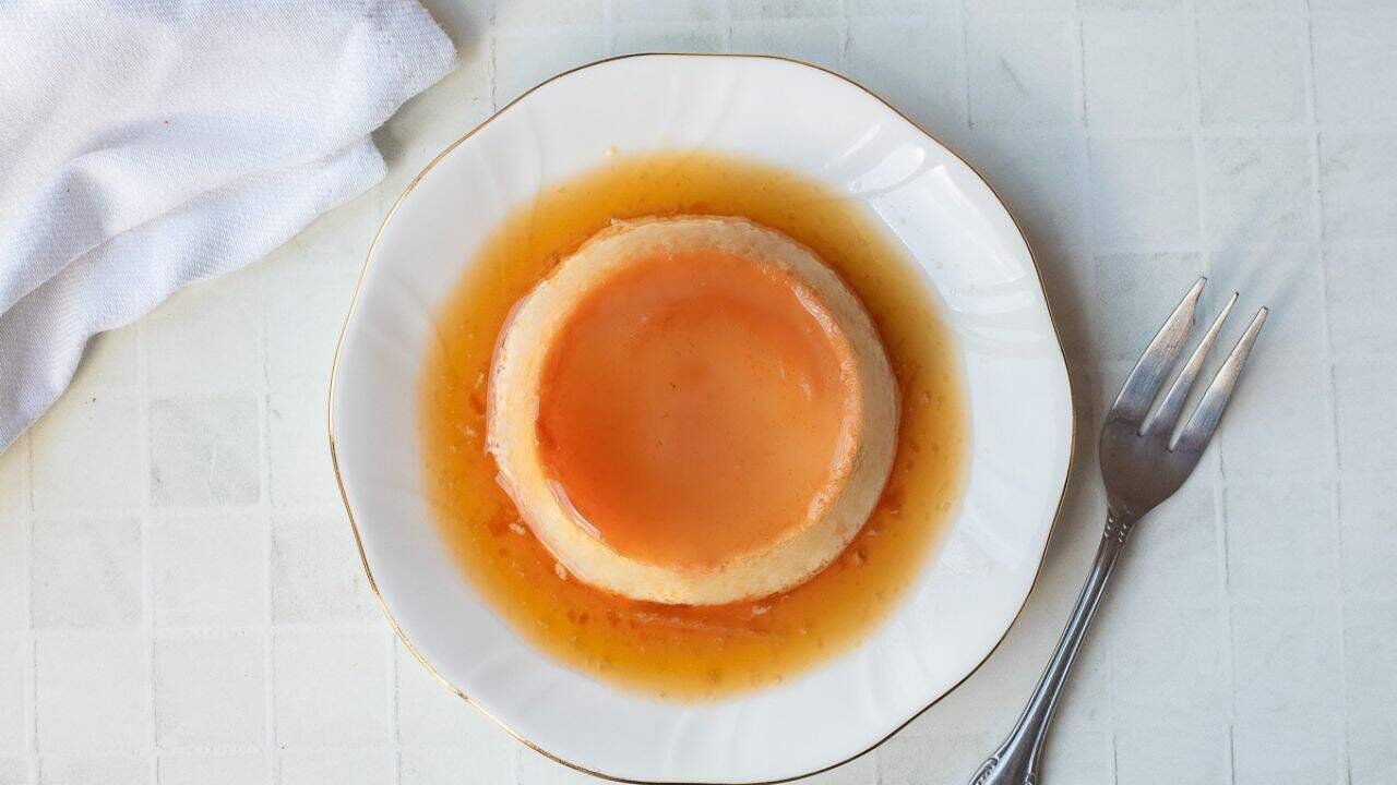 A plate with a serving of Vietnamese Egg Flan, topped with caramel sauce, with a fork holding a piece.