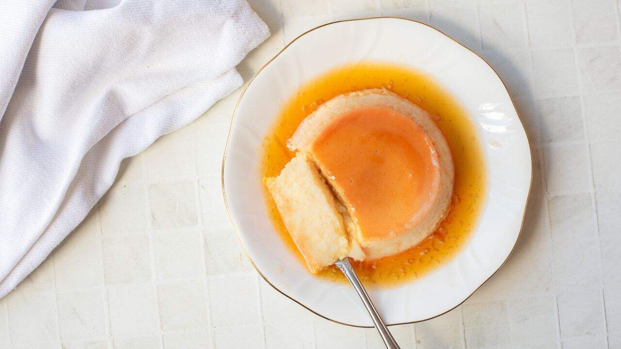 A plate with a serving of Vietnamese Egg Flan, topped with caramel sauce, with a fork holding a piece.