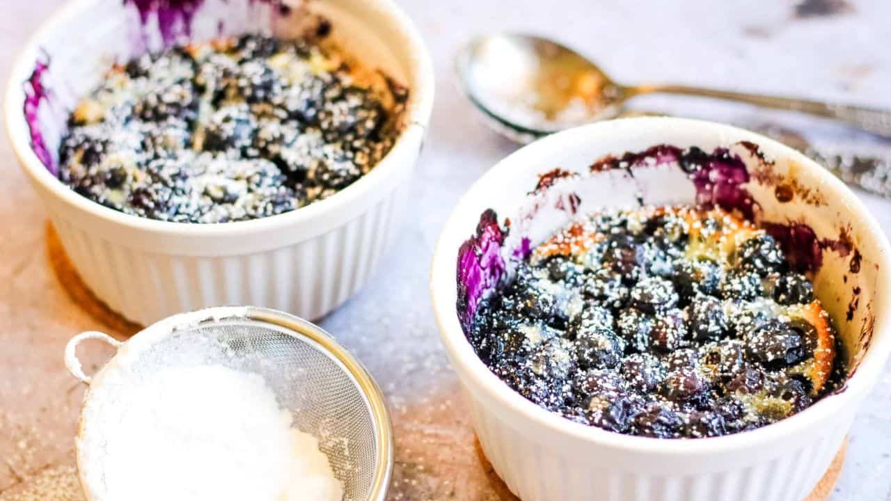 Low angle shot of 2 white ramekins filled with blueberry clafoutis.