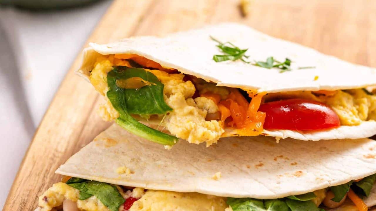 An image of two breakfast quesadillas on a wooden cutting board.
