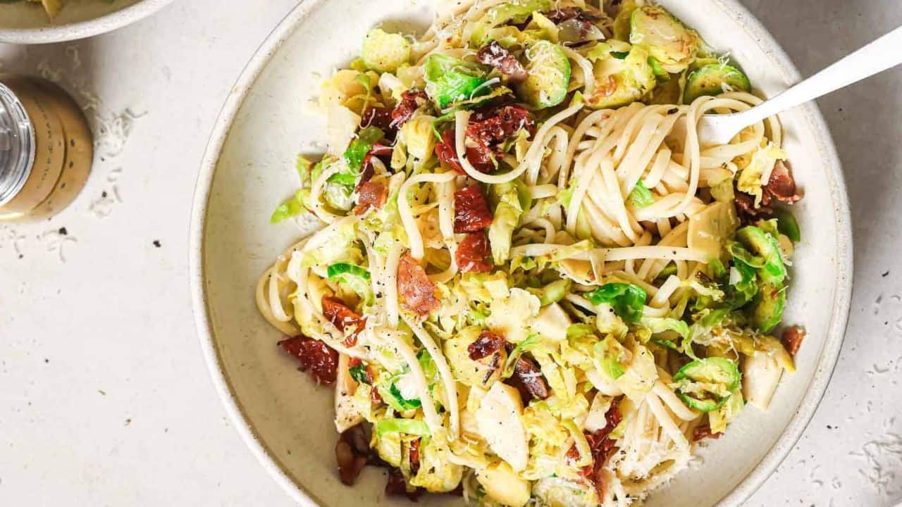 A bowl of pasta with bacon and brussels sprouts.