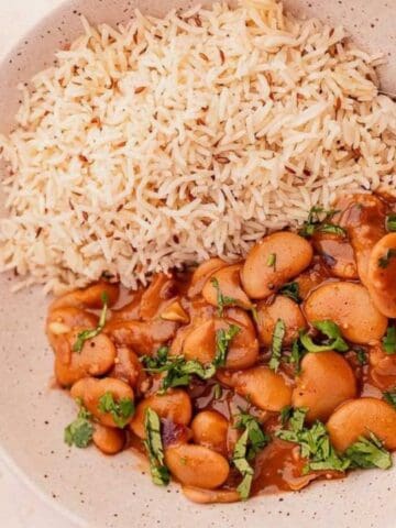 A bowl of cooked rice served with a saucy butter bean curry, garnished with chopped herbs, with a spoon in the bowl.