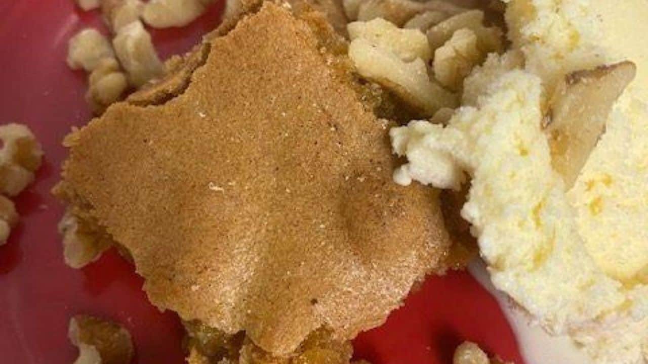 Butterscotch brownie with walnuts and vanilla ice cream on red plate.