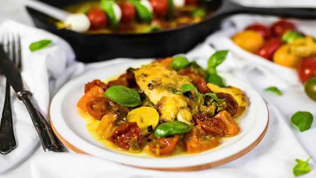 Caprese Chicken served on a plate with fresh basil, surrounded by vibrant ingredients and a skillet in the background.