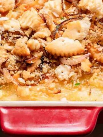 A baked casserole topped with crushed crackers, browned onions, and fresh parsley in a red rectangular dish.