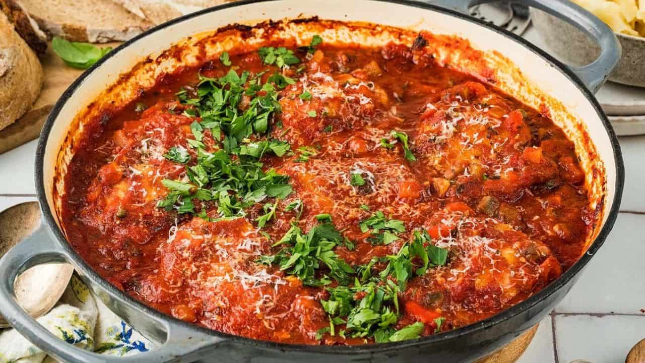 A round skillet filled with chicken breasts cooked in tomato sauce, topped with fresh chopped parsley and grated cheese.