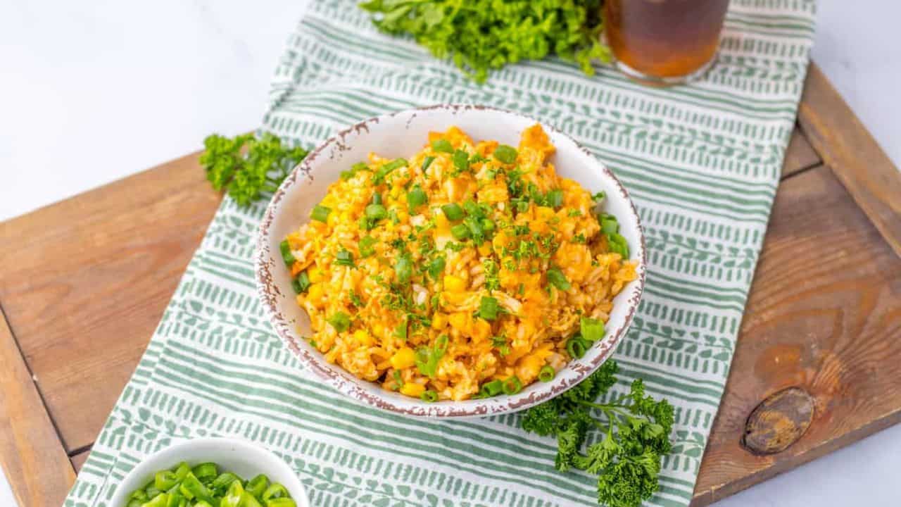 A bowl of rice with corn and herbs on a striped cloth with garnishes on the side.