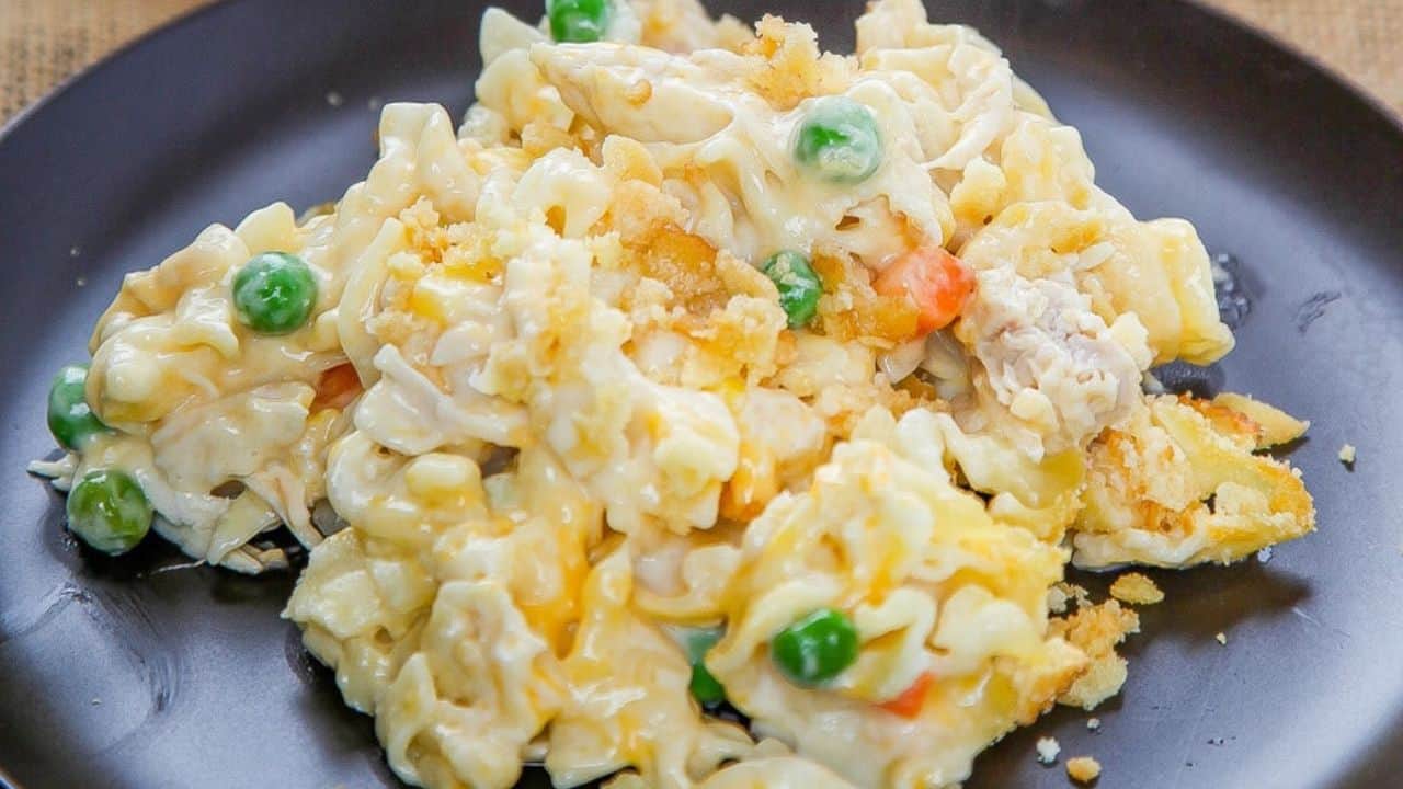 A serving of creamy pasta casserole with peas, carrots, and a crumb topping on a dark plate.