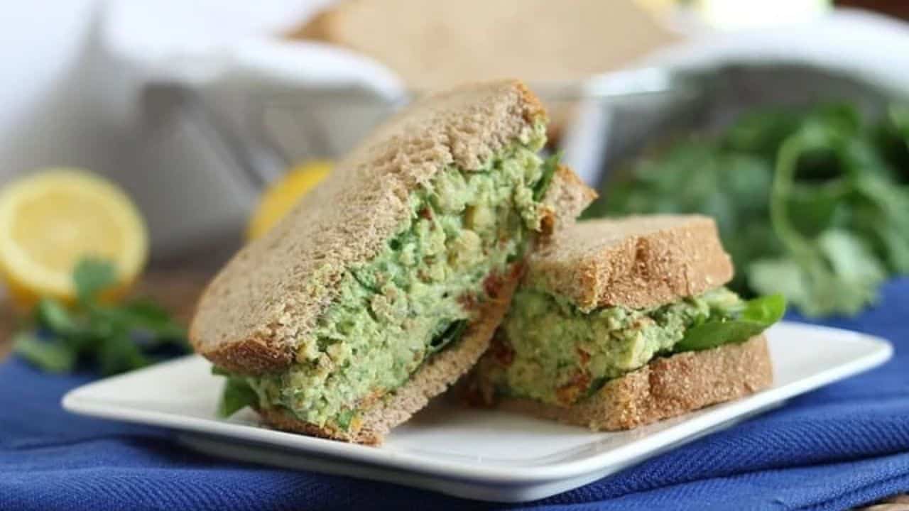Chickpea pesto sandwich cut in half and stacked on a white plate.