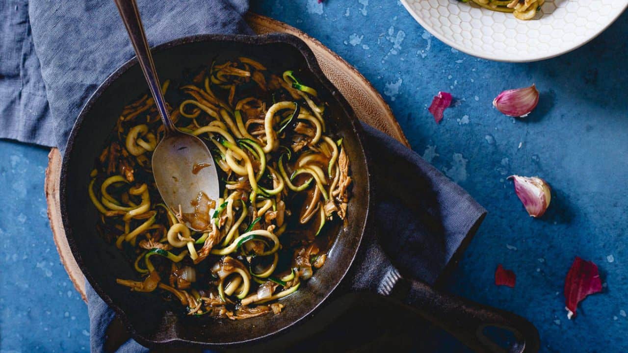 Zucchini noodles with shredded chicken in a stir fry sauce in cast iron skillet.