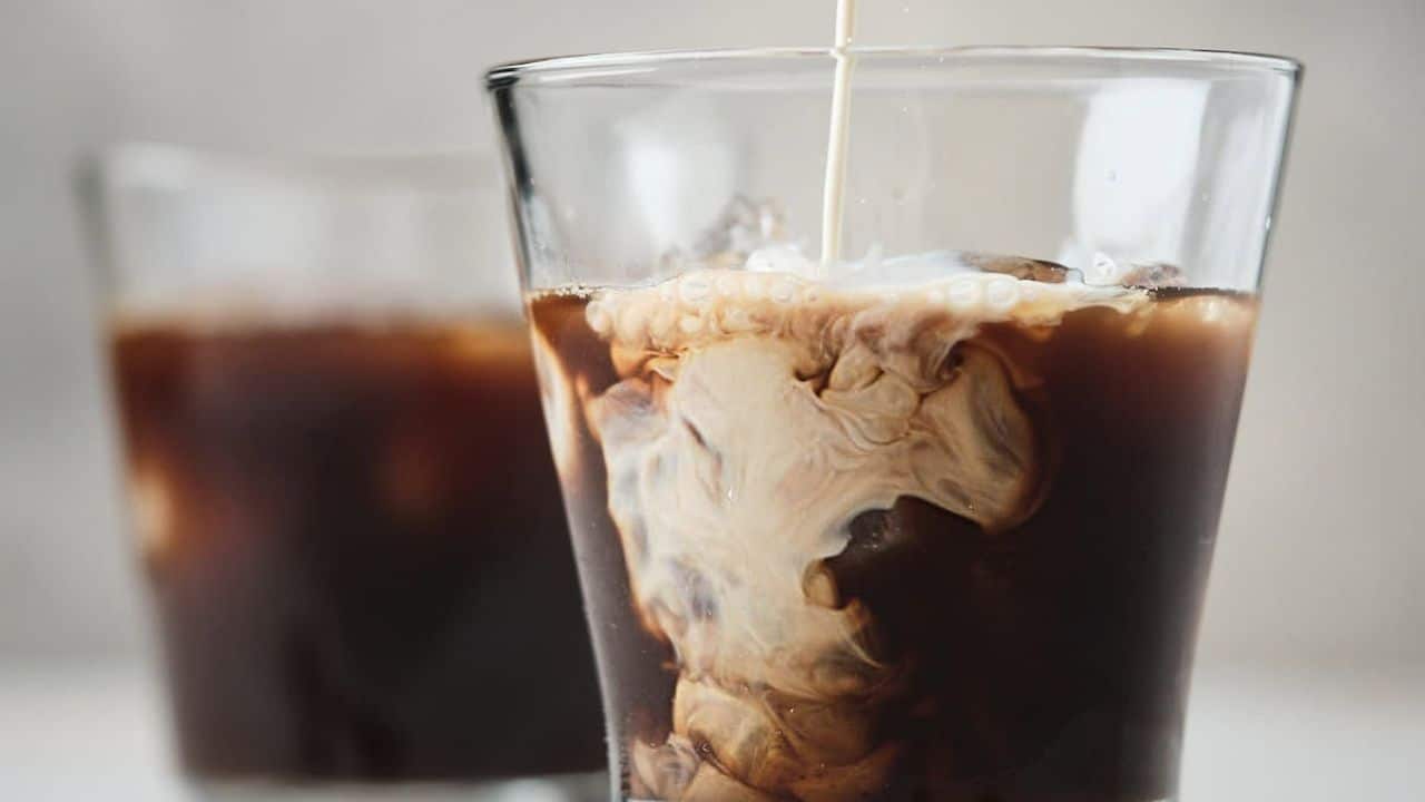 Two glasses of iced cold brew coffee with cream and coffee beans.