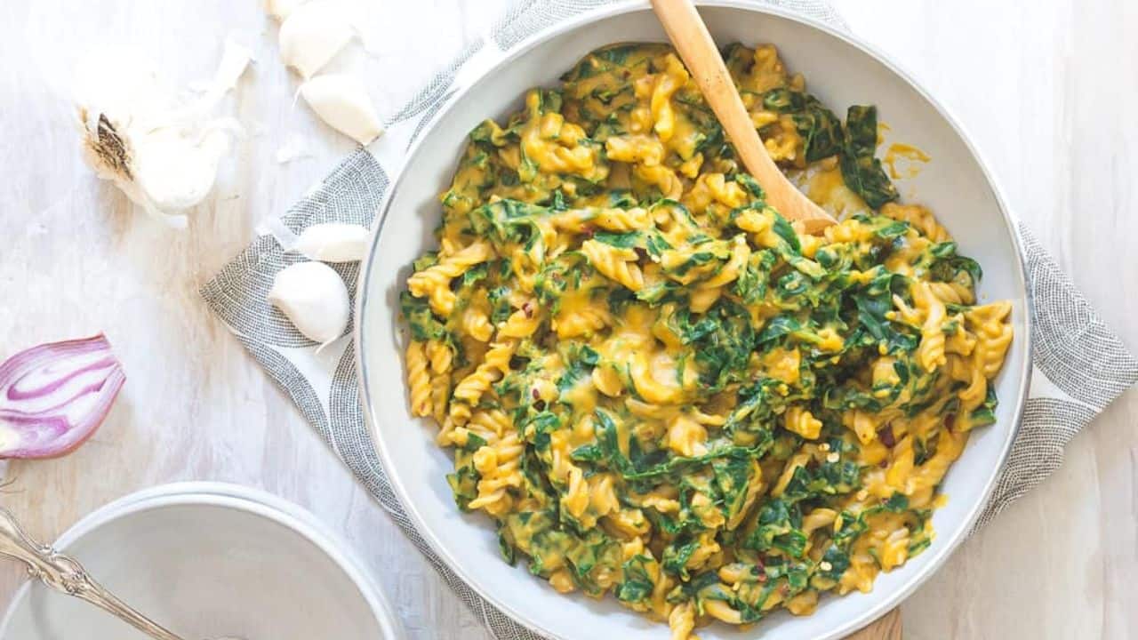 Creamy pumpkin pasta with garlic and tuscan kale in a bowl with a spoon.