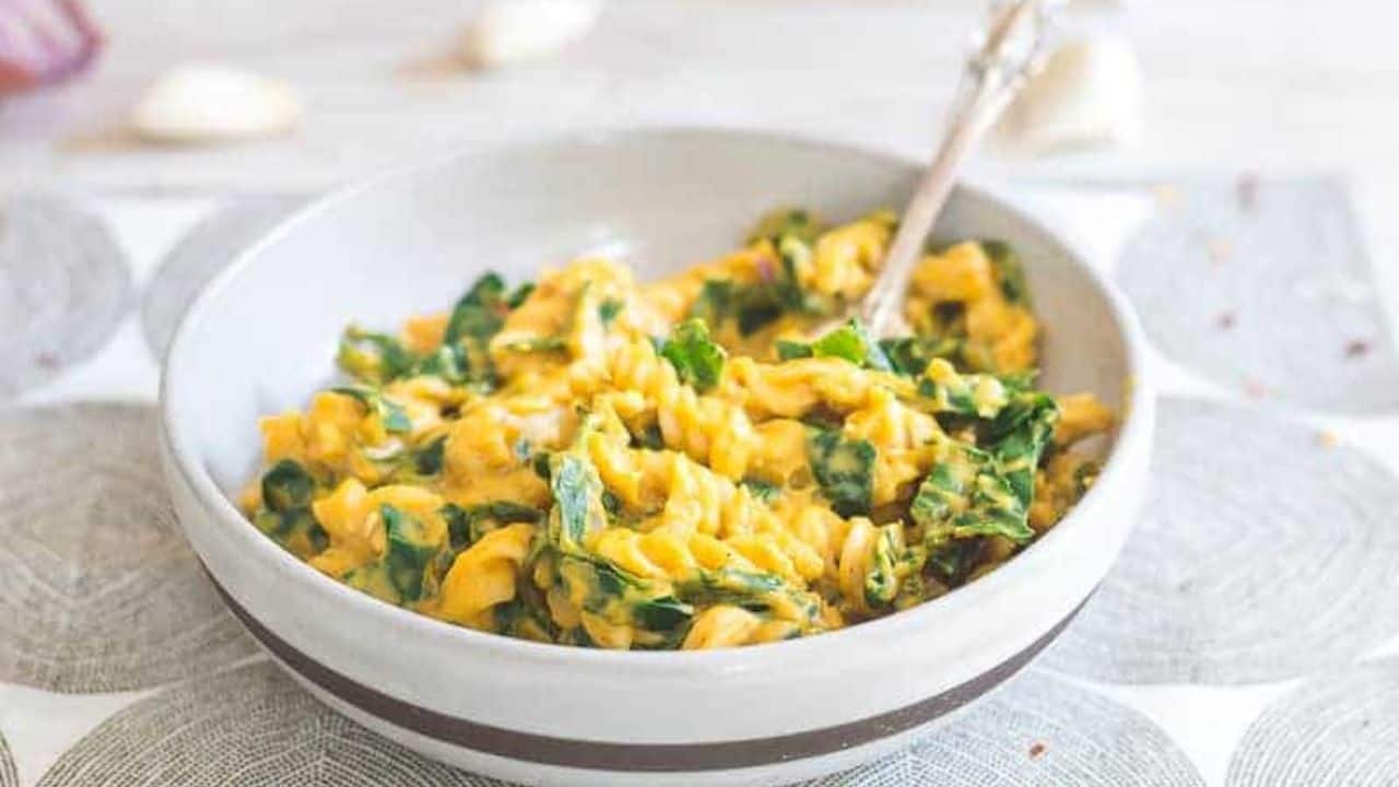 Creamy pumpkin pasta with garlic and tuscan kale in a bowl with a spoon.